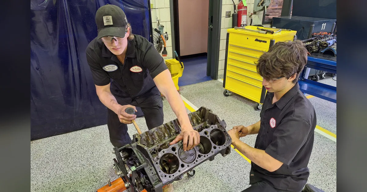 Two Arapahoe Community College students in black shop shirts working on a bare V8 engine block on an engine stand