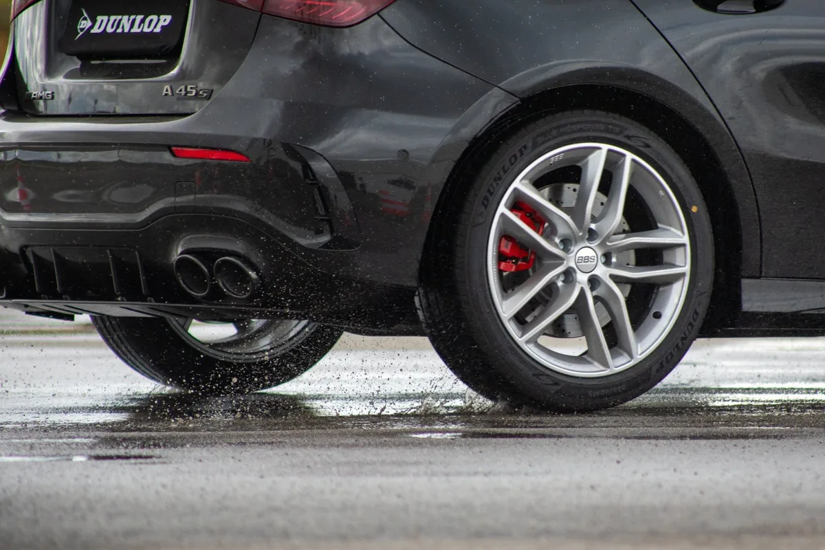 Dark hatchback on Dunlop tyres driving through spray on a wet test surface