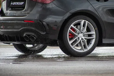 Dark hatchback on Dunlop tyres driving through spray on a wet test surface