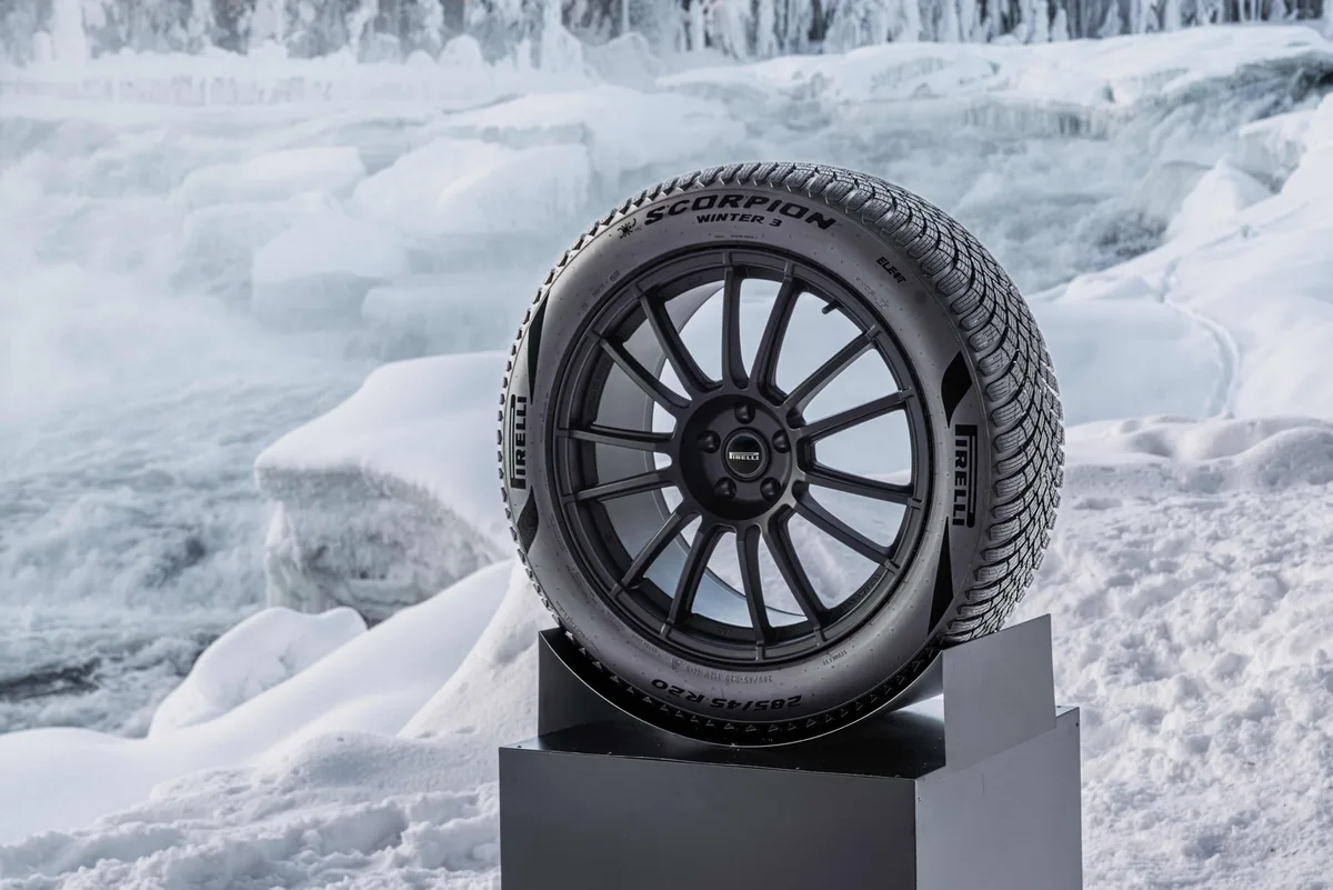 Pirelli Scorpion Winter 3 tire on a dark wheel, displayed on a plinth in a snowy landscape