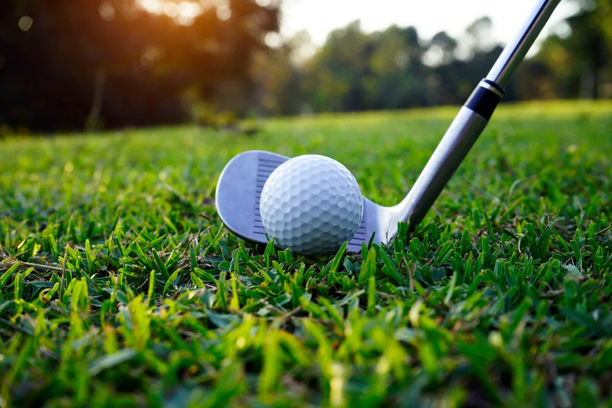 Golf club addressing a ball on a tee on a sunlit fairway