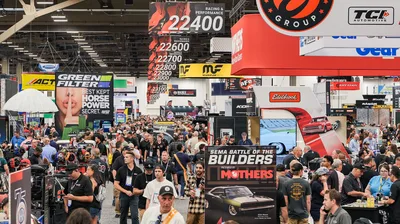 Crowds of attendees walking a busy aisle lined with exhibitor booths on the SEMA Show floor at the Las Vegas Convention Center