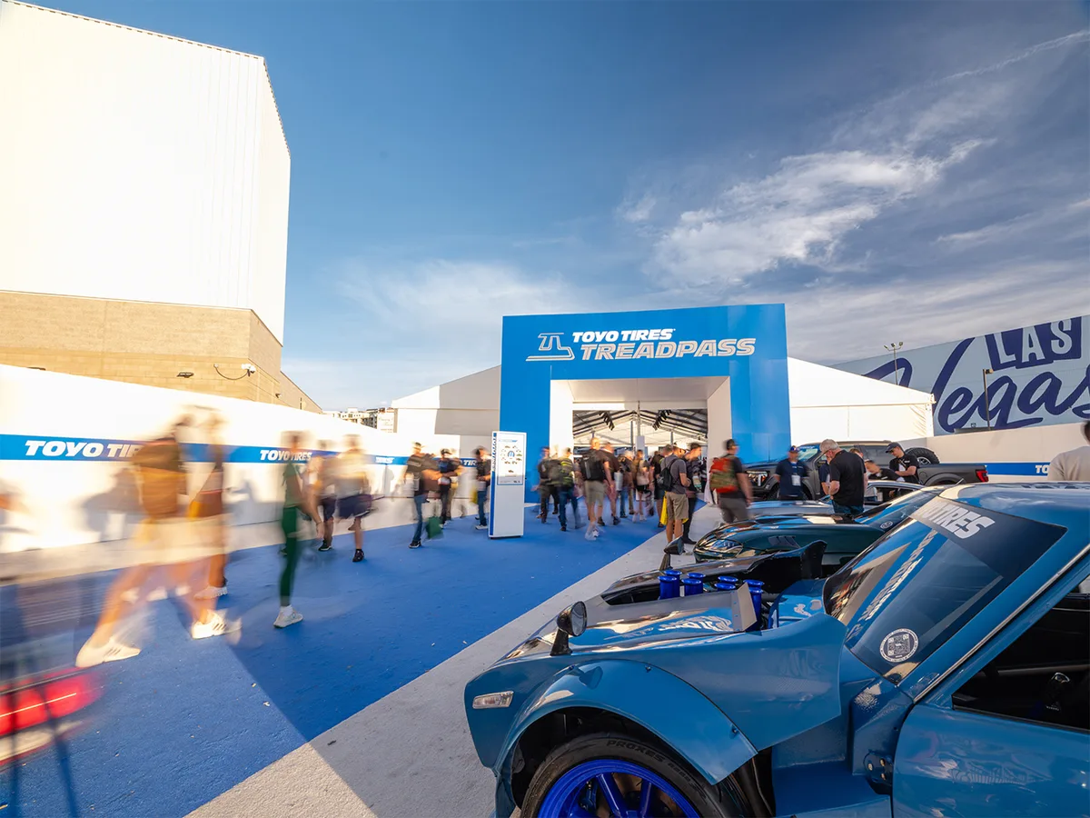 Toyo Tires Treadpass entrance arch at the SEMA Show in Las Vegas with attendees walking past a blue custom car on Toyo Proxes tires