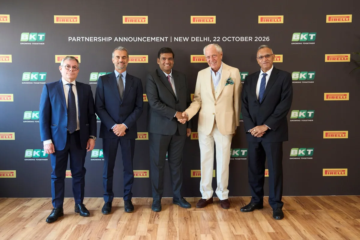 Pirelli and BKT executives shake hands at their partnership announcement in New Delhi in front of a Pirelli and BKT branded backdrop.