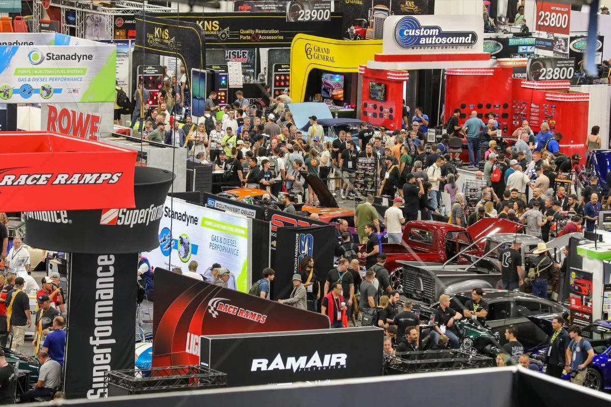 An overhead view of a crowded SEMA Show aisle in Las Vegas, with attendees walking between exhibitor booths and show vehicles.