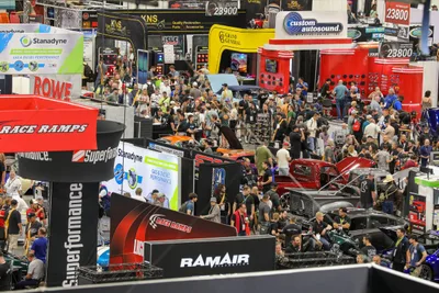 An overhead view of a crowded SEMA Show aisle in Las Vegas, with attendees walking between exhibitor booths and show vehicles.