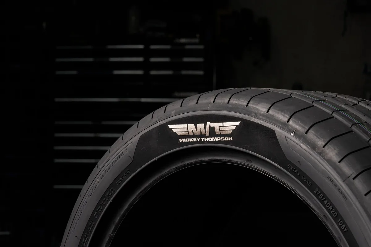 Close-up of a Mickey Thompson 275/40R20 ultra-high-performance tire with a foil M/T Mickey Thompson sidewall logo against a dark garage background