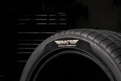 Close-up of a Mickey Thompson 275/40R20 ultra-high-performance tire with a foil M/T Mickey Thompson sidewall logo against a dark garage background